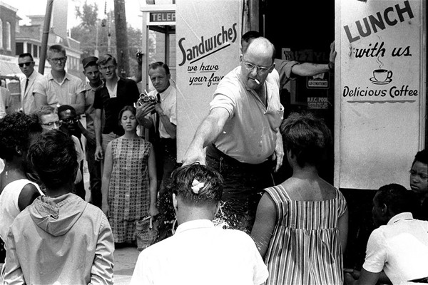 Robert Fahsenfeldt, owner of a segregated lunchroom in the racially tense Eastern Shore community of Cambridge, Maryland, douses a white integrationist with water, on July 8, 1963. The integrationist, Edward Dickerson, was among three white and eight Black protesters who knelt on the sidewalk in front of the restaurant to sing freedom songs. A raw egg, which Fahsenfeldt had broken over Dickerson's head moments earlier, still is visible on the back of Dickerson's head. 