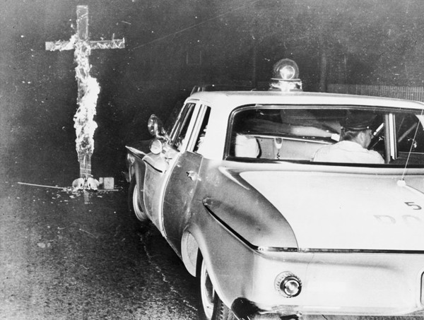 Chicago police move in to knock down a burning cross in front of a home, after an Black family moved into a previously all white neighborhood, on the 6th consecutive night of disturbances, on August 3, 1963.